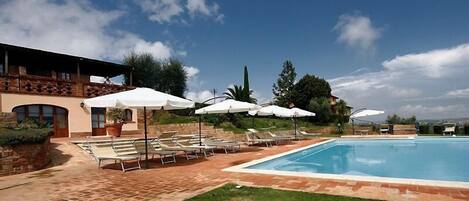 A pool area with lounge chairs and umbrellas, a stone building, and a clear sky.