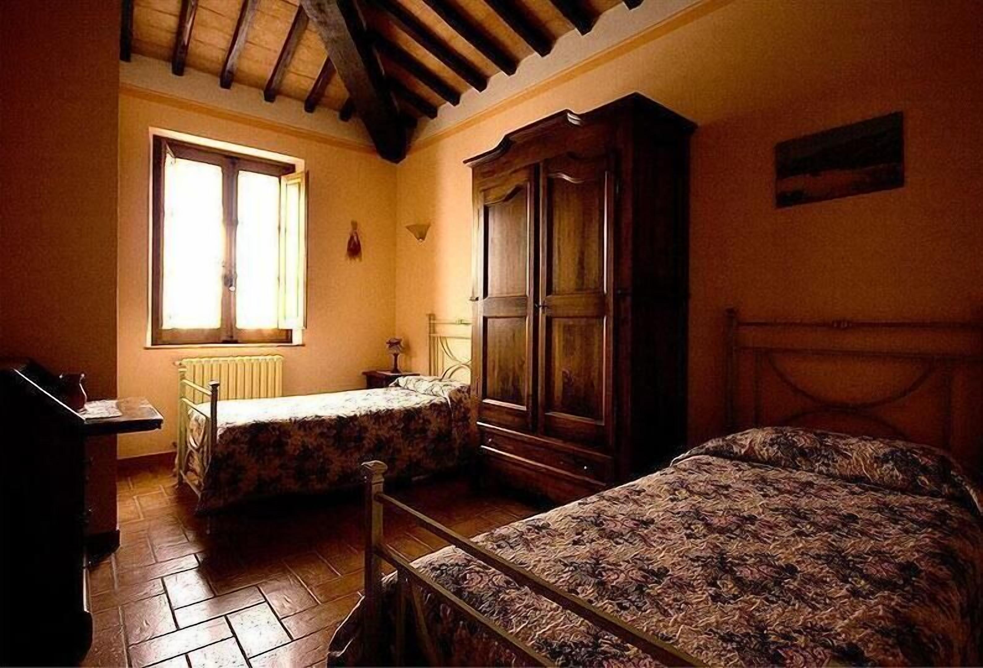 A bedroom with two beds, a wooden wardrobe, a radiator, and a window with curtains.