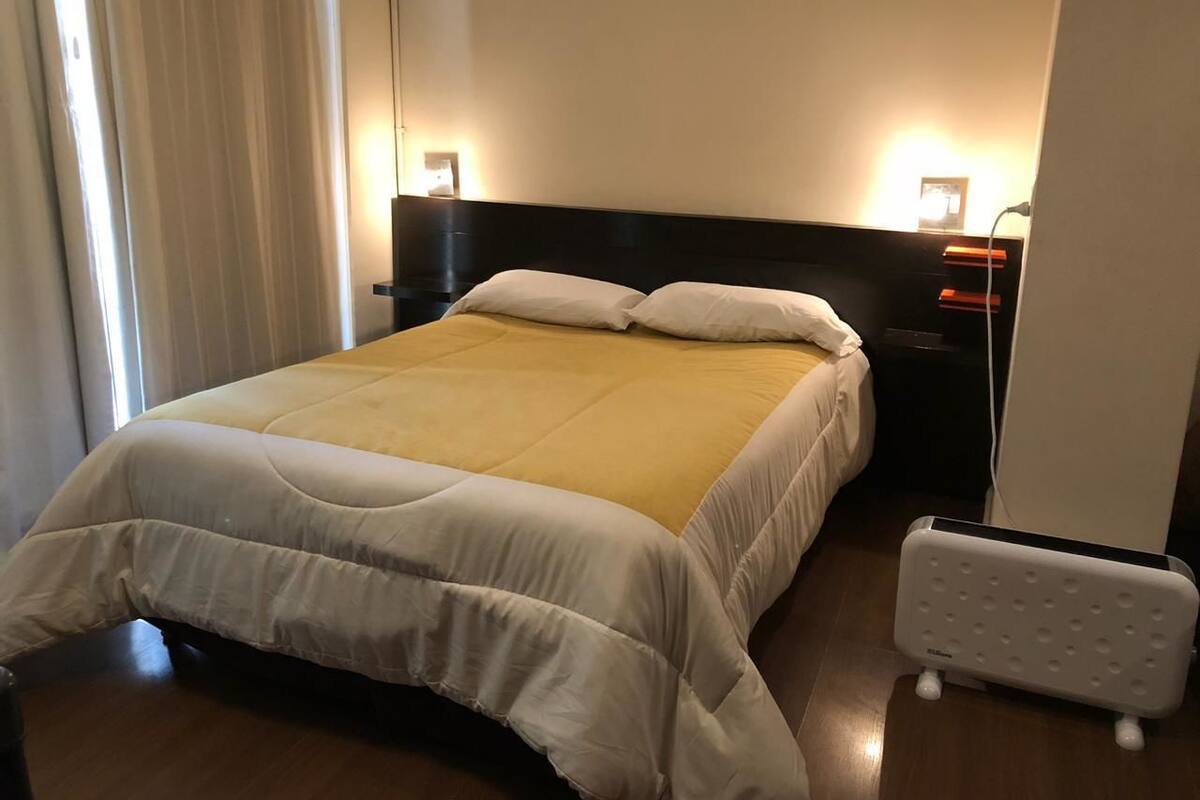 A neatly made bed with a white and yellow bedspread, a black headboard, and bedside lamps.