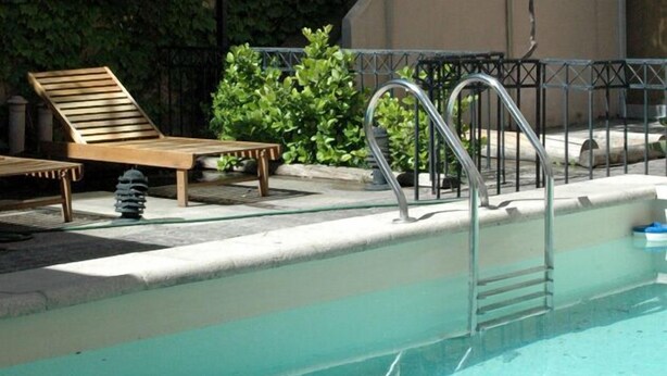 Una piscina con una escalera metálica, sillones de madera para tomar el sol y un pequeño banco.
