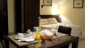 Una habitación de hotel con una cama bien tendida, una mesa de comedor con alimentos para el desayuno y una lámpara de noche.