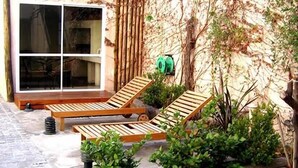Un patio con dos sillones de madera, una mesita y un ventanal con vistas a muebles de interior.