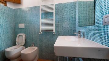 Un baño con inodoro, bidé y lavamanos, con azulejos azules y blancos.