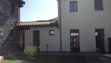 En toetages bygning med en stenfassade og et tegltag. Der er et lille haveareal med en plantepotte og en metalstol.