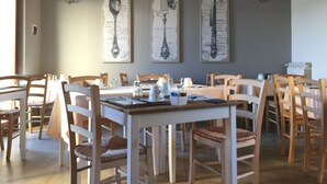 Un comedor con mesas y sillas de madera, mantel blanco y tres paneles con la carta enmarcados en la pared.