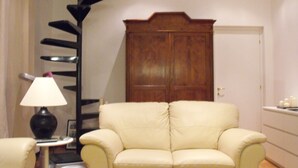 Una sala de estar con un sofá color beige, una mesita auxiliar con lámpara, un aparador de madera y una puerta.