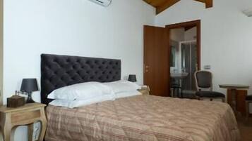 A bedroom with a large bed, wooden ceiling beams, a small desk, and an open door leading to another room.