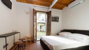 Un dormitorio con cama, un escritorio, dos taburetes y una puerta que da a un espacio exterior.