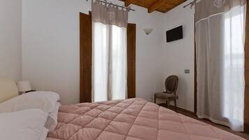 A bedroom with a large bed, a chair, a TV, and a window with curtains.
