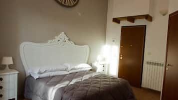 A bedroom with a large bed, a wall clock, a bedside table with a lamp, and a door.