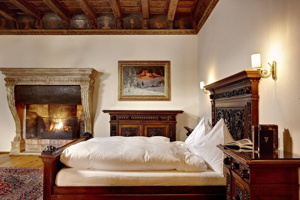 A bedroom with a fireplace, a bed, a nightstand, and a wall-mounted lamp.