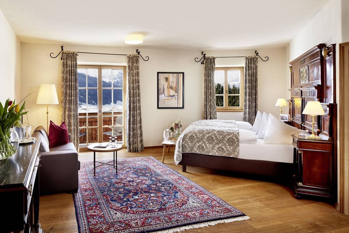 A hotel room with a large bed, a sofa, a coffee table, and a view of mountains through the window.
