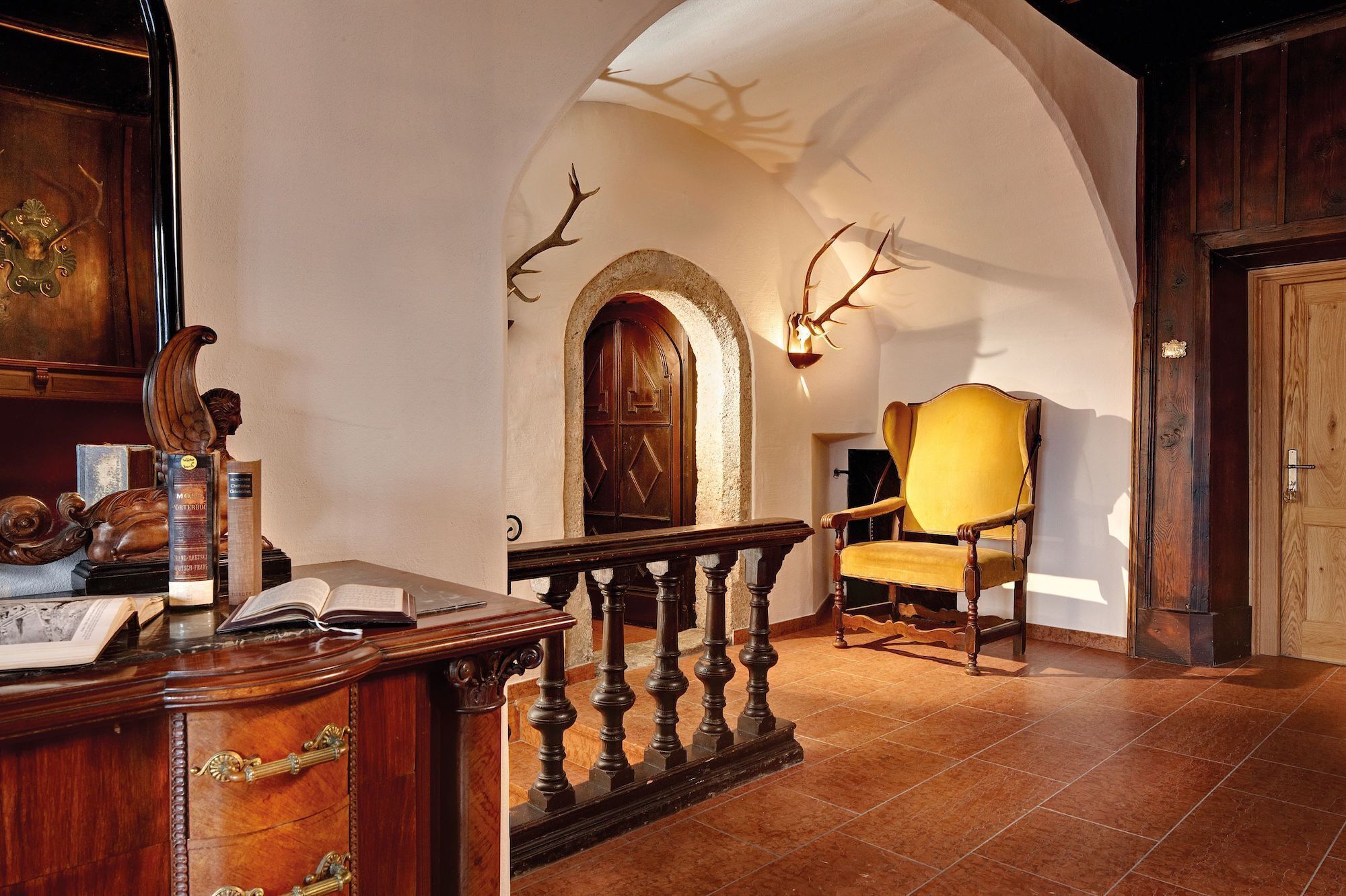 A room with a wooden desk, books, a yellow armchair, a fireplace, and a wooden door.