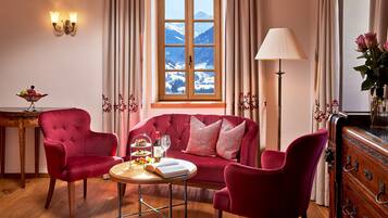 A cozy room with a red sofa, two matching armchairs, a wooden coffee table, and a view of snow-capped mountains through a large window.