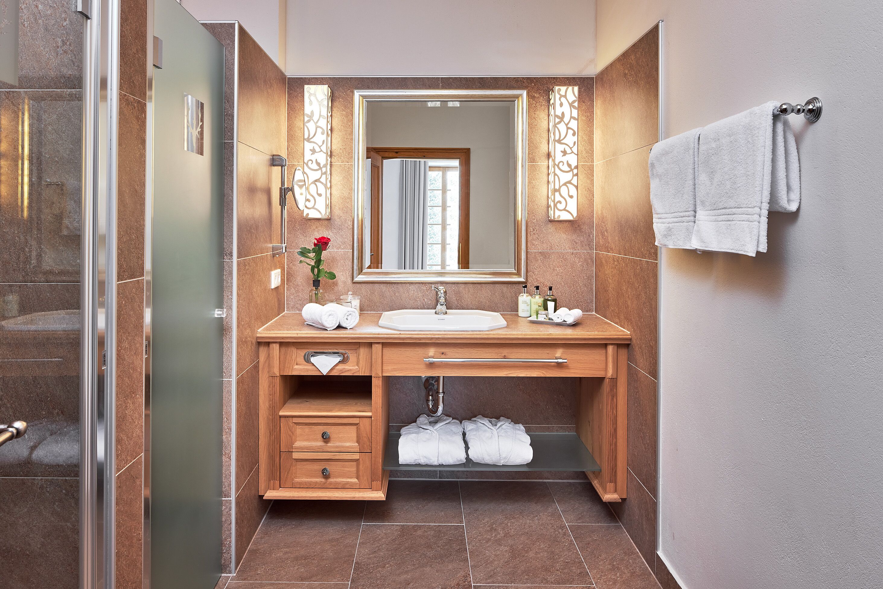 A modern bathroom with a glass shower enclosure, a wooden vanity with a sink, and a large mirror.