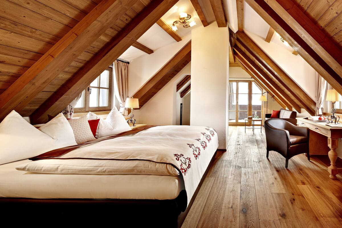 A bedroom with a large bed, wooden beams, a desk, and a chair.