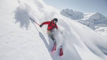 A person skiing down a snowy slope with mountains in the background.