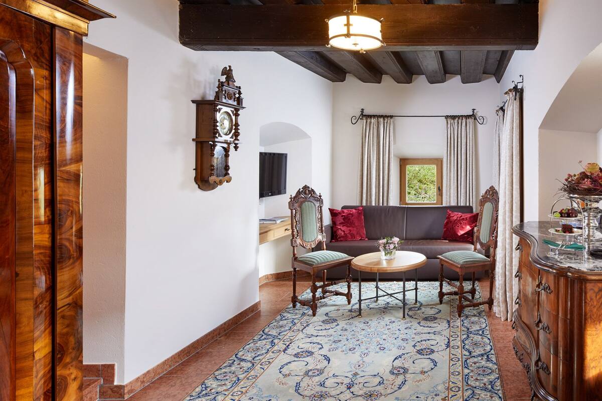 A traditional room with a wooden cabinet, a clock, a sofa, a table, and a patterned rug.