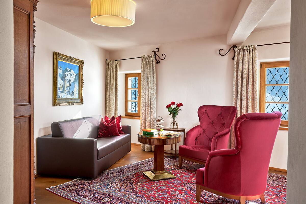 A living room with a dark sofa, a red armchair, a round wooden coffee table, and a patterned rug.