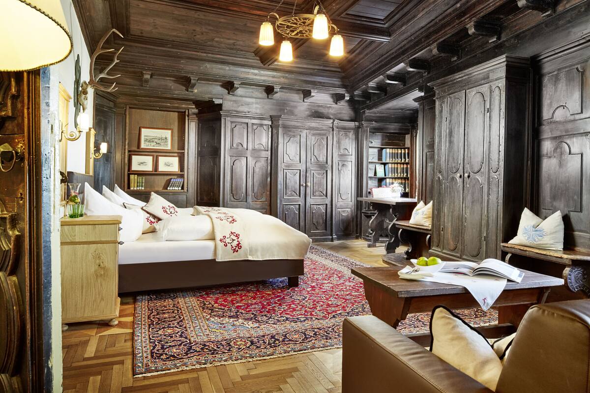 A traditional room with a large bed, wooden paneling, a chandelier, and a bookshelf.