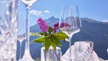 A table set with clear glassware and a vase with purple flowers against a mountainous backdrop.