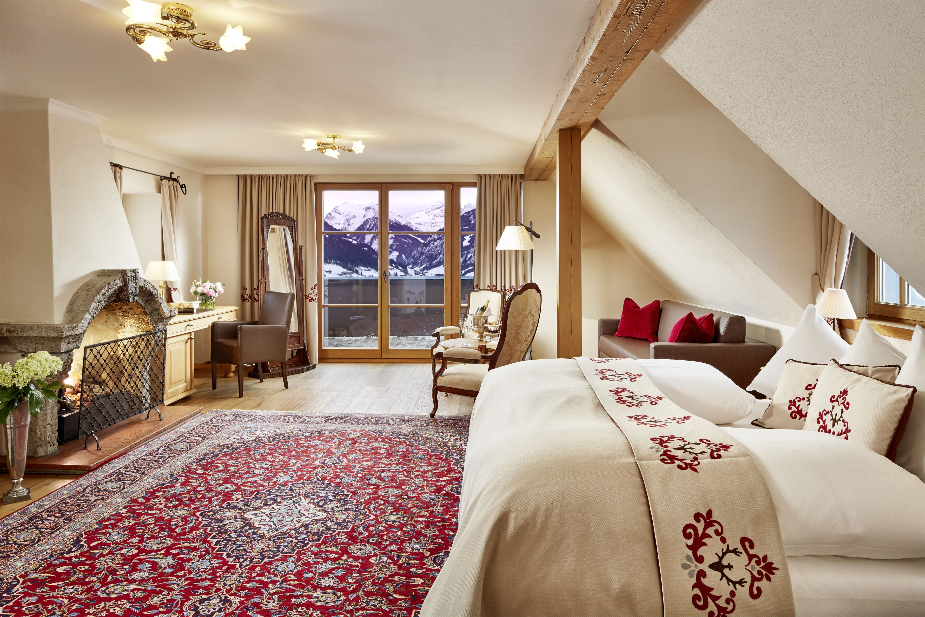 A hotel room with a large bed, a desk, a chair, a fireplace, and a view of mountains through the window.