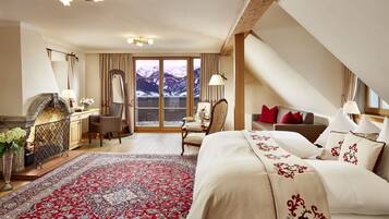 A hotel room with a large bed, a desk, a chair, a fireplace, and a view of mountains through the window.