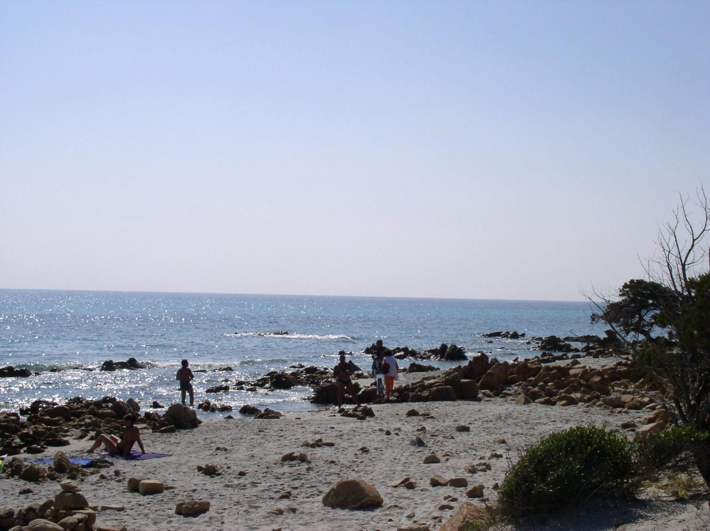 A rocky beach with clear blue water and a few people.
