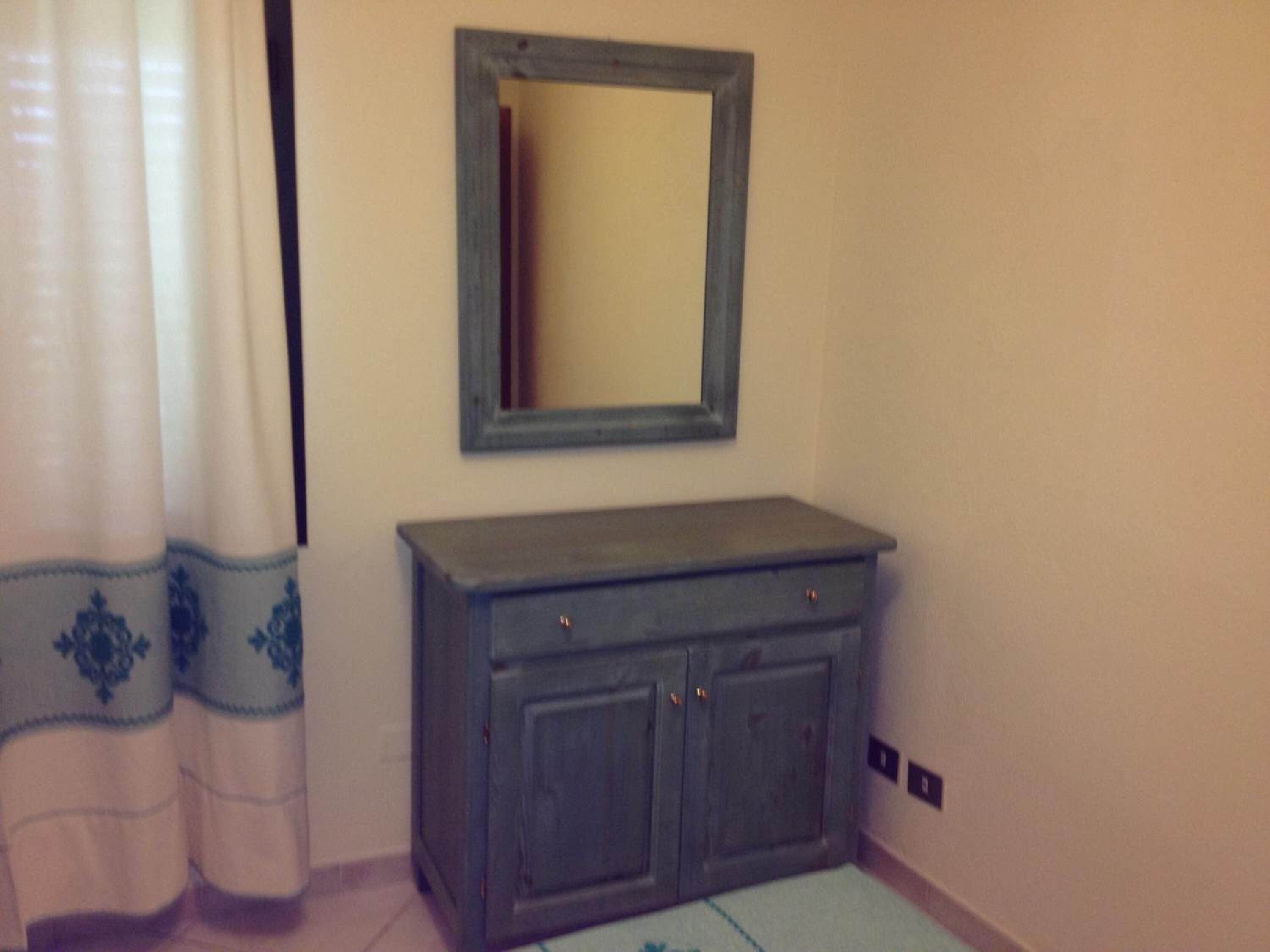 A bathroom with a grey cabinet, a mirror, and a curtain with a blue pattern.