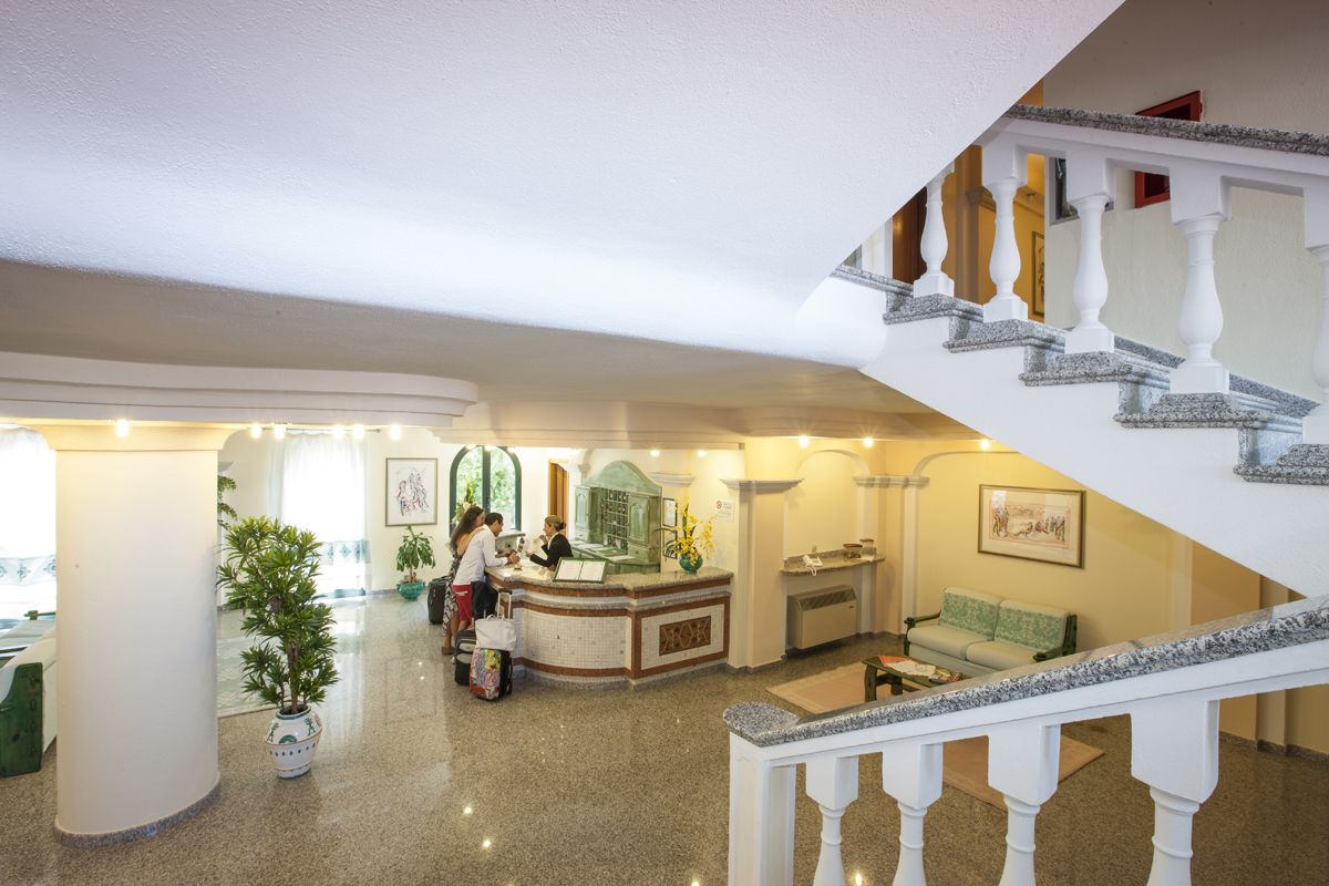 A hotel lobby with a reception desk, a staircase, and a seating area.
