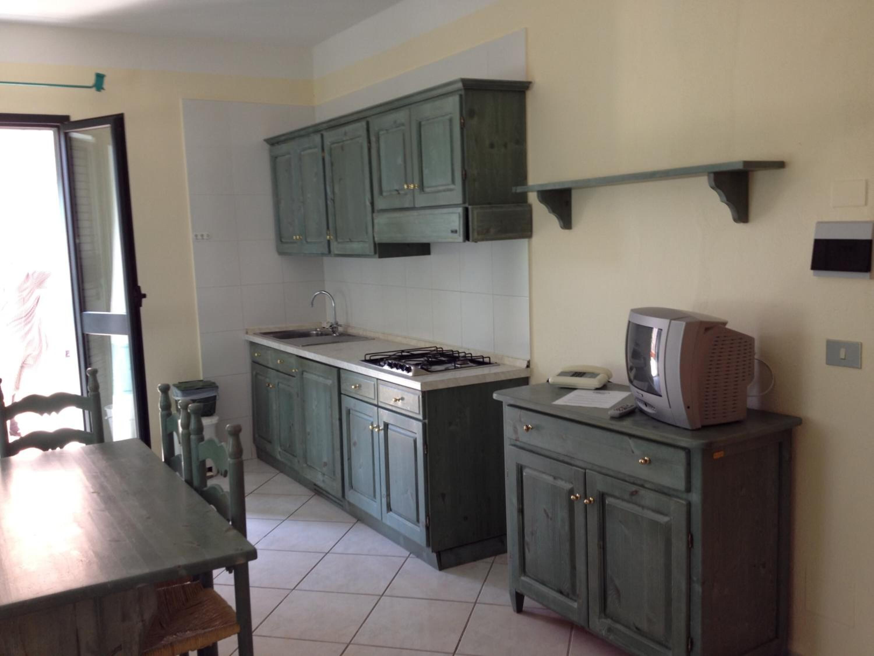 Une cuisine avec des meubles de rangement verts, une cuisinière à gaz, un évier et une petite table.