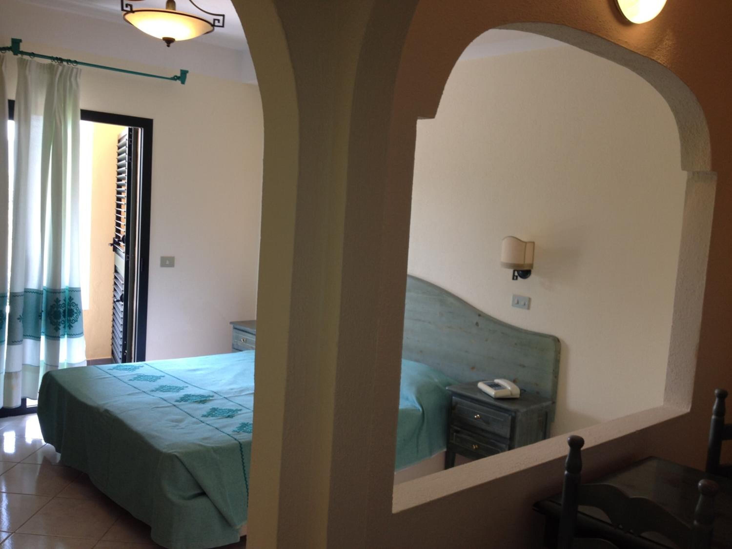 A bedroom with a bed, a nightstand, a mirror, and a window with curtains.