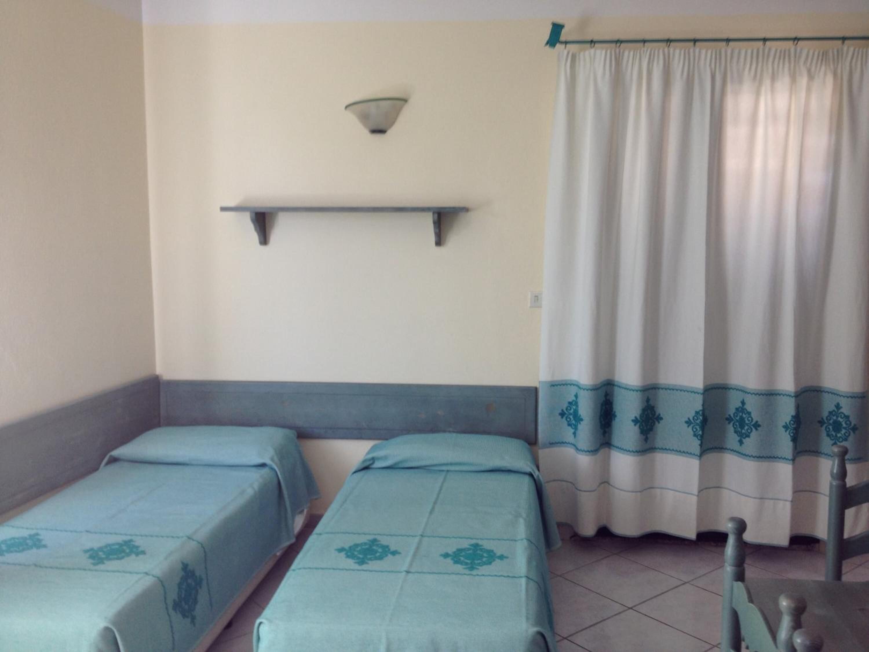 Una habitación con dos camas, un estante en la pared, una cortina y una silla.