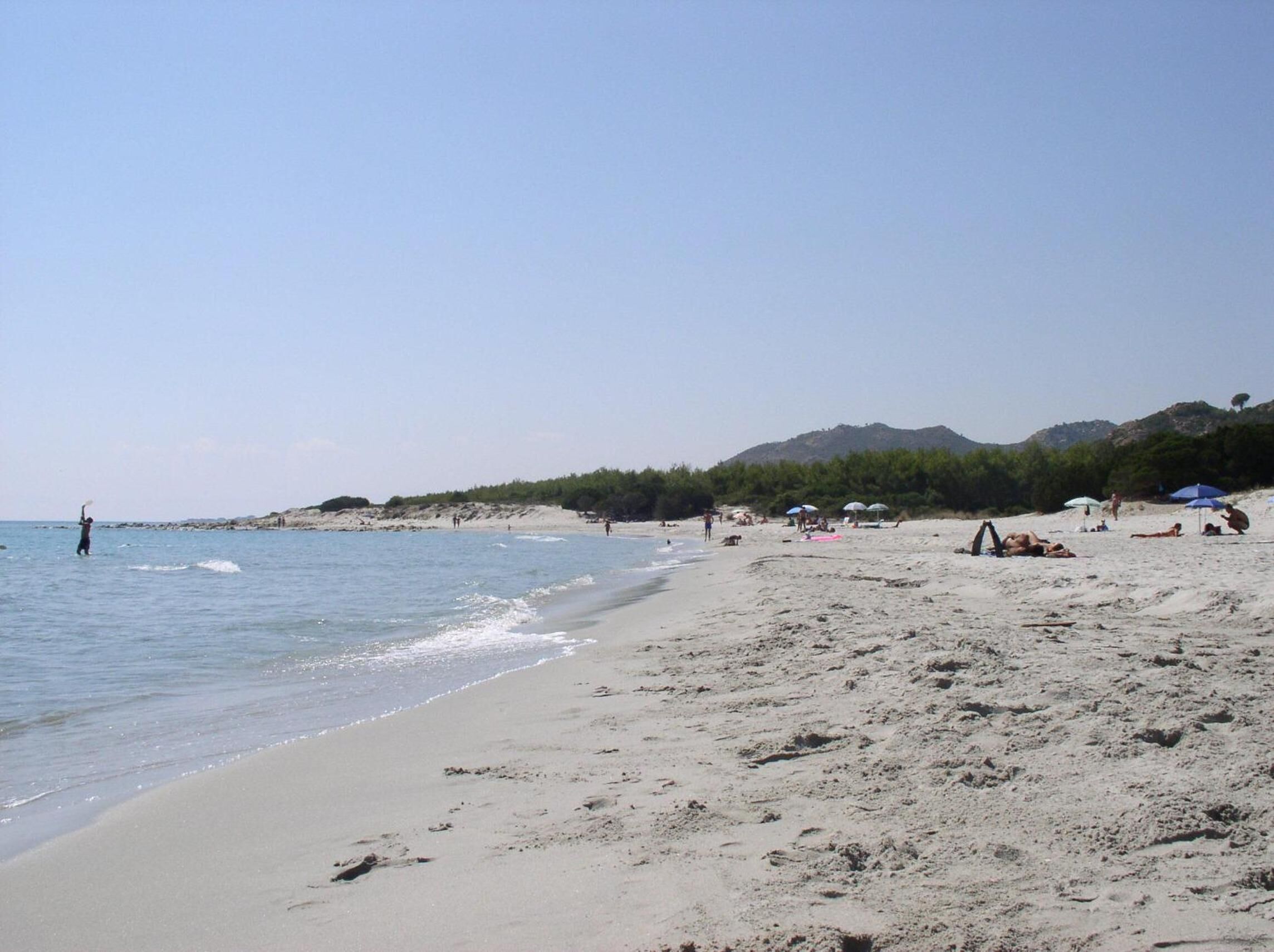 A beach with clear skies, sandy shore, and a few people.