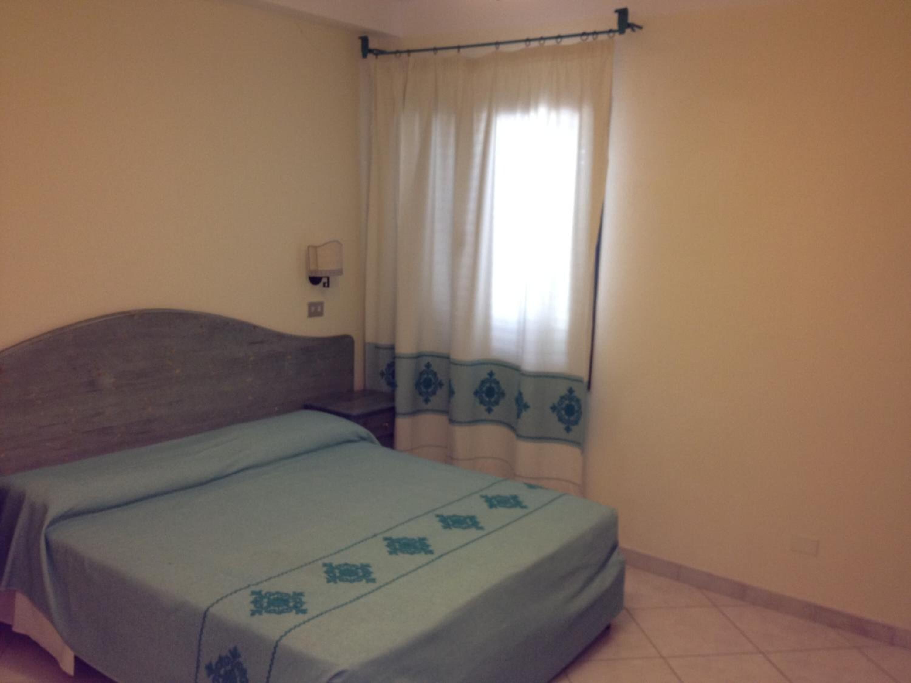 A single bed with a headboard, a bedside table, and a window with curtains.