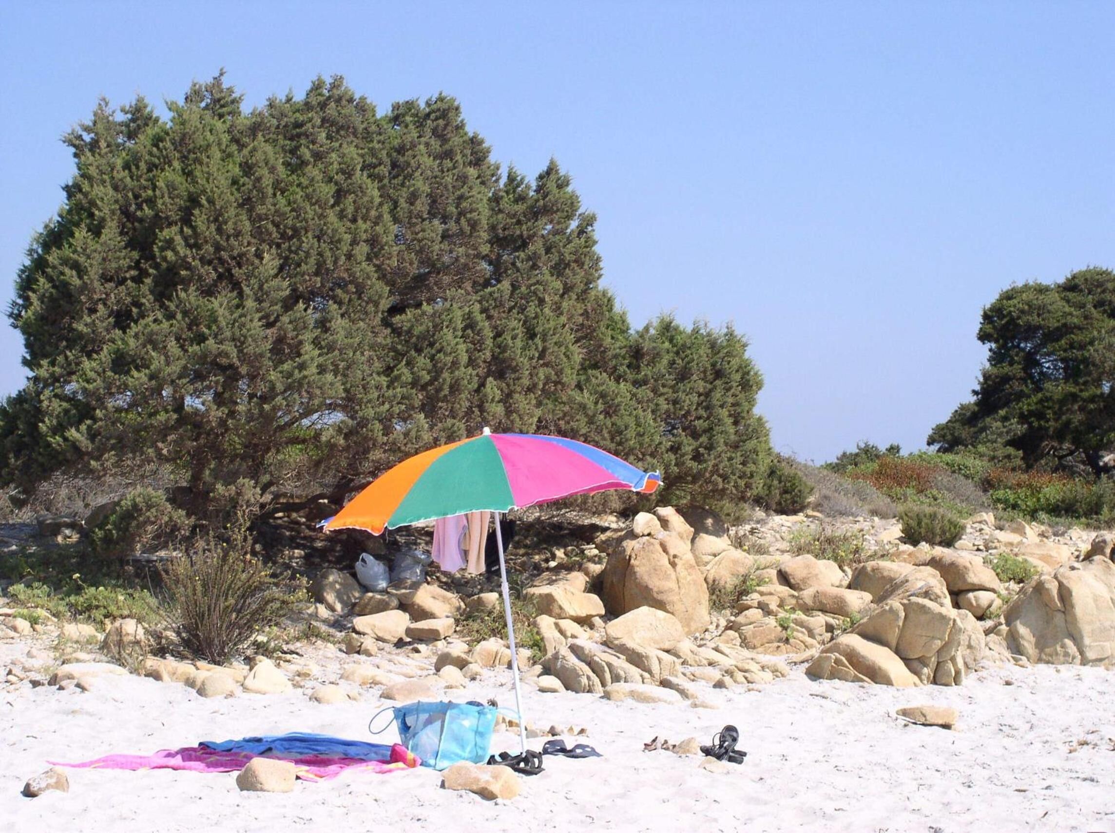 Una spiaggia con un ombrellone colorato, una sedia da spiaggia e una borsa sulla sabbia.