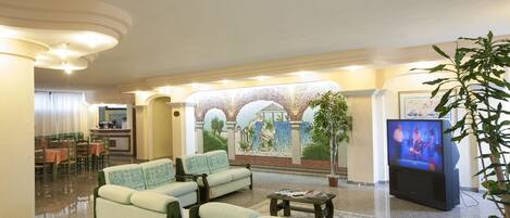 Un vestíbulo de hotel con una zona de estar, un televisor y un mural.