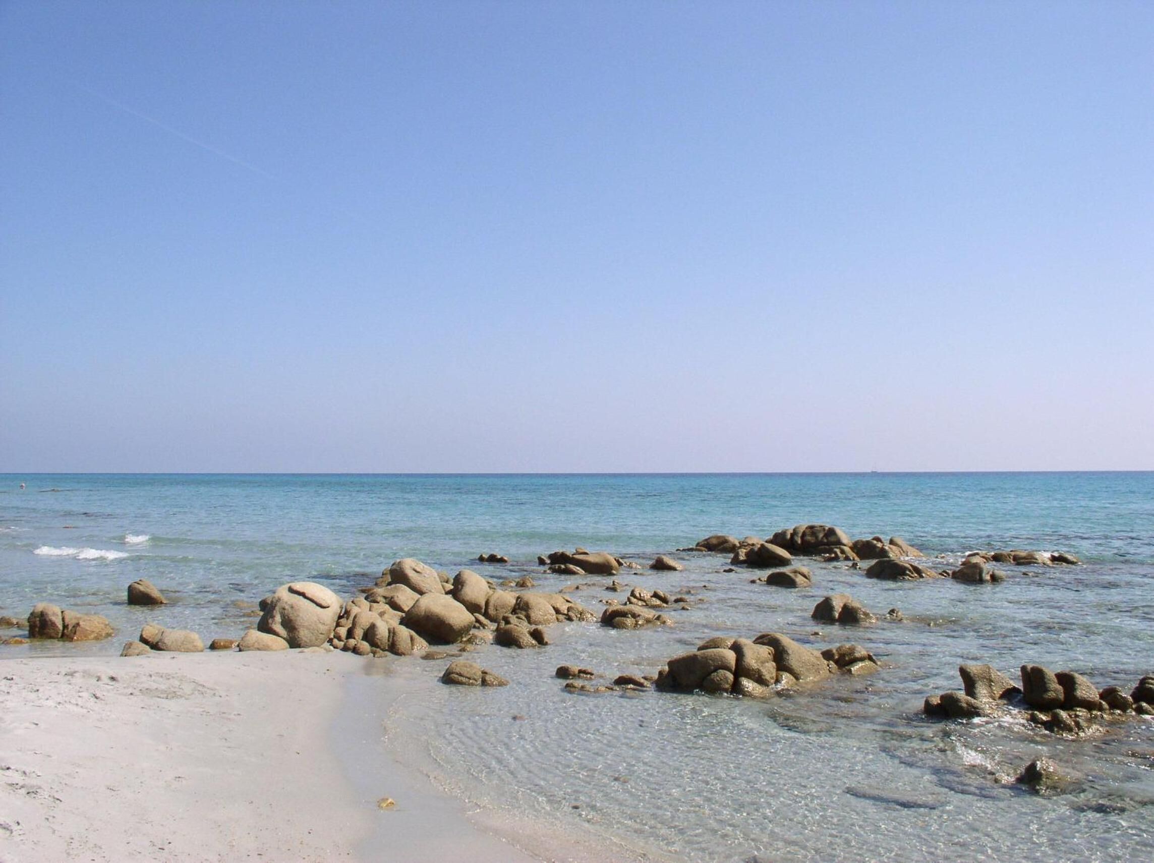 Una spiaggia con acque limpide e grandi rocce in primo piano.