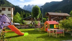 A playground with a slide and climbing structures, surrounded by houses and a mountain backdrop. - Hotel Al Sole (Auronzo di Cadore)