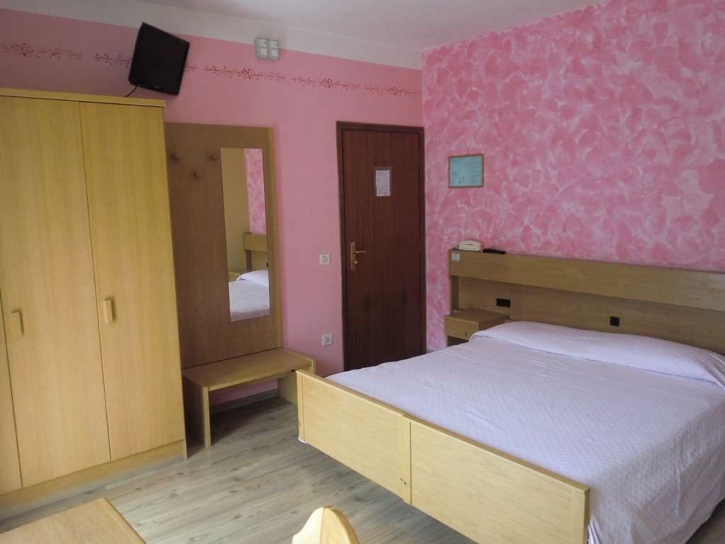 A bedroom with a wooden bed, a wardrobe, a bench, and a door.