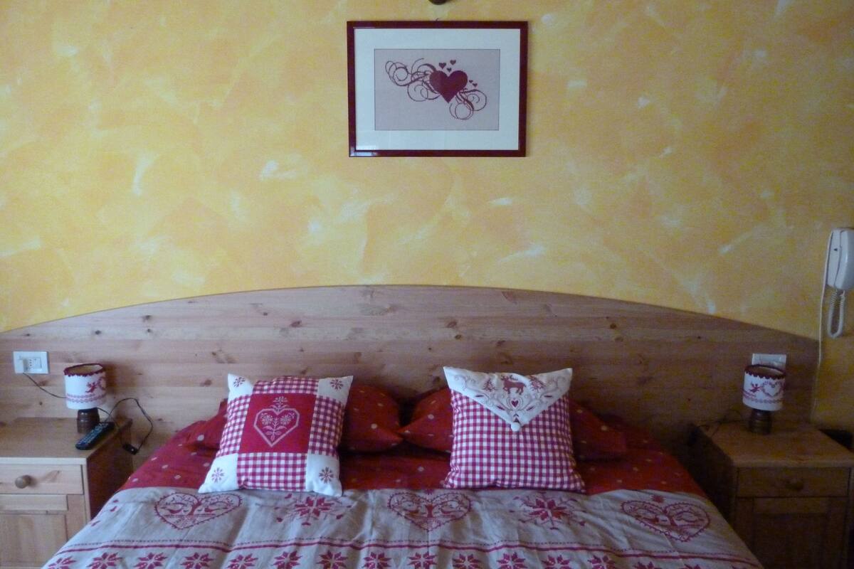 A bedroom with a wooden headboard, a bed with red and white checkered bedding, two bedside tables with lamps, and a framed picture on the wall.
