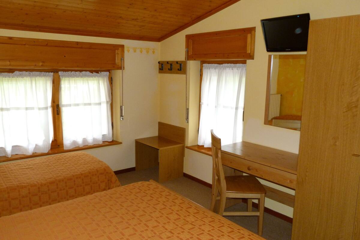 A room with two beds, a wooden desk, a chair, a television, and a window with curtains.