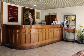 Un comptoir d’accueil avec un revêtement en bois, une enseigne encadrée au-dessus, et une vitrine en verre contenant des objets, située à droite.