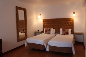 Une chambre d’hôtel avec deux lits simples, un grand miroir, des lampes de chevet et un plancher en bois.