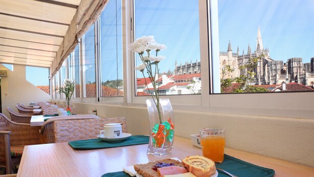 Une table de petit-déjeuner avec une assiette de nourriture, un verre de jus d’orange et un vase rempli de fleurs.
