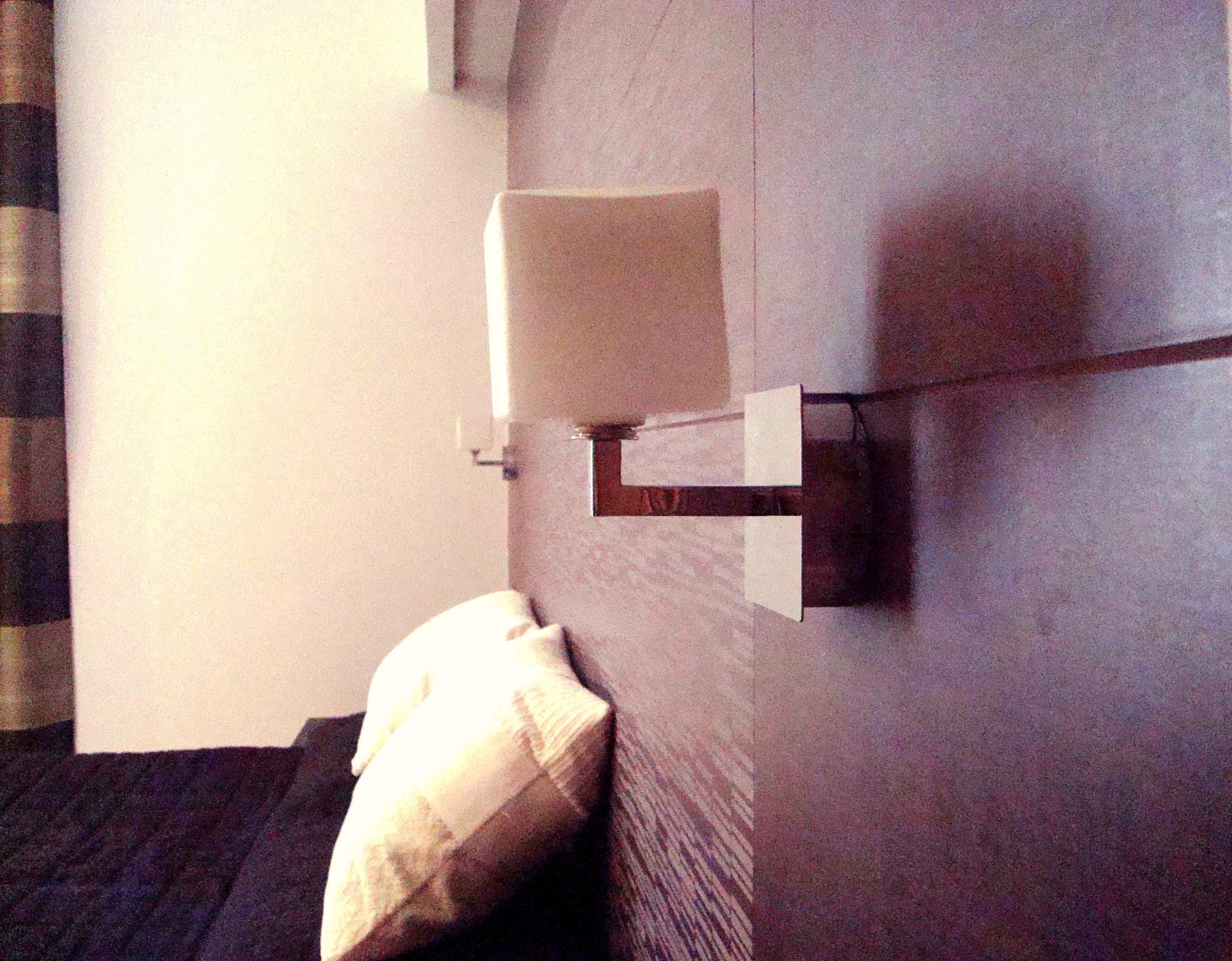 Ein Hotelzimmer mit Bett, Kissen, einer Wandleuchte und einem kleinen Fenster.