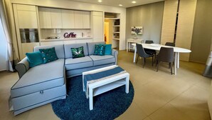 A modern living room with a grey sofa, a coffee sign, a dining table with chairs, and a kitchen area in the background. - Interno 5 (Rome)