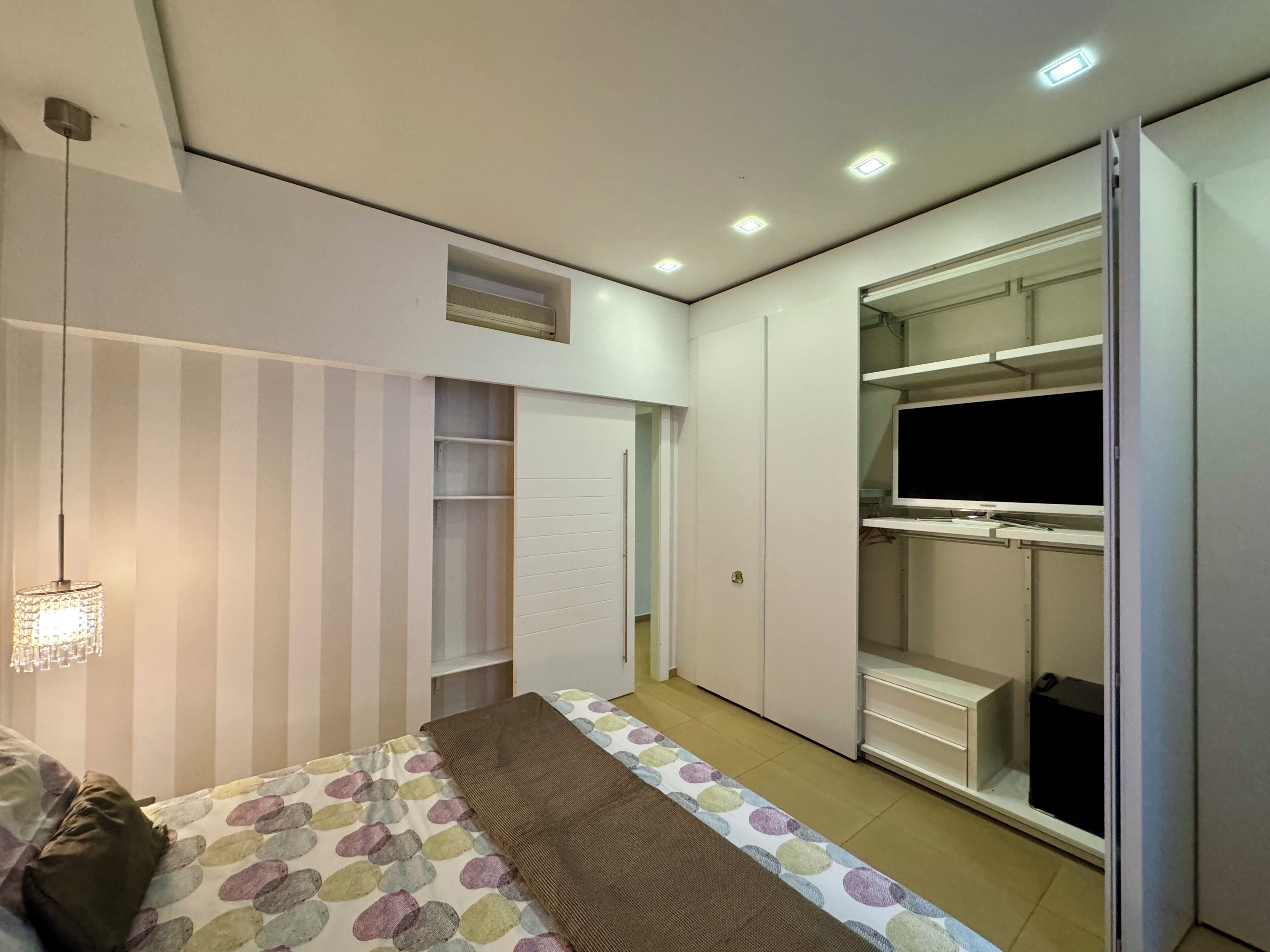 A bedroom with a bed, a TV, a wardrobe, and a hanging light fixture.