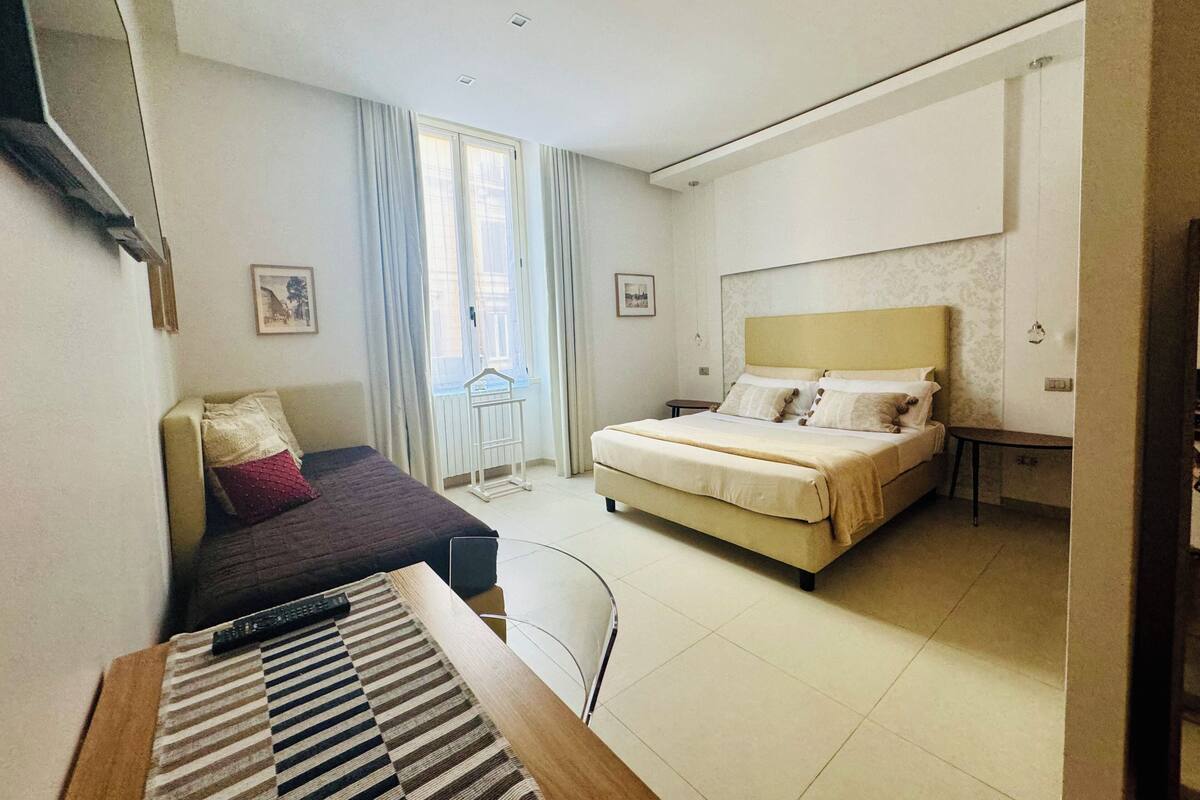 Una camera d'albergo con un letto, una scrivania, una sedia, una finestra con tende e un tavolino.