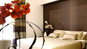 A modern hotel room with a large bed, a nightstand, a vase with flowers, and a view of the city. - Interno 5 (Rome)